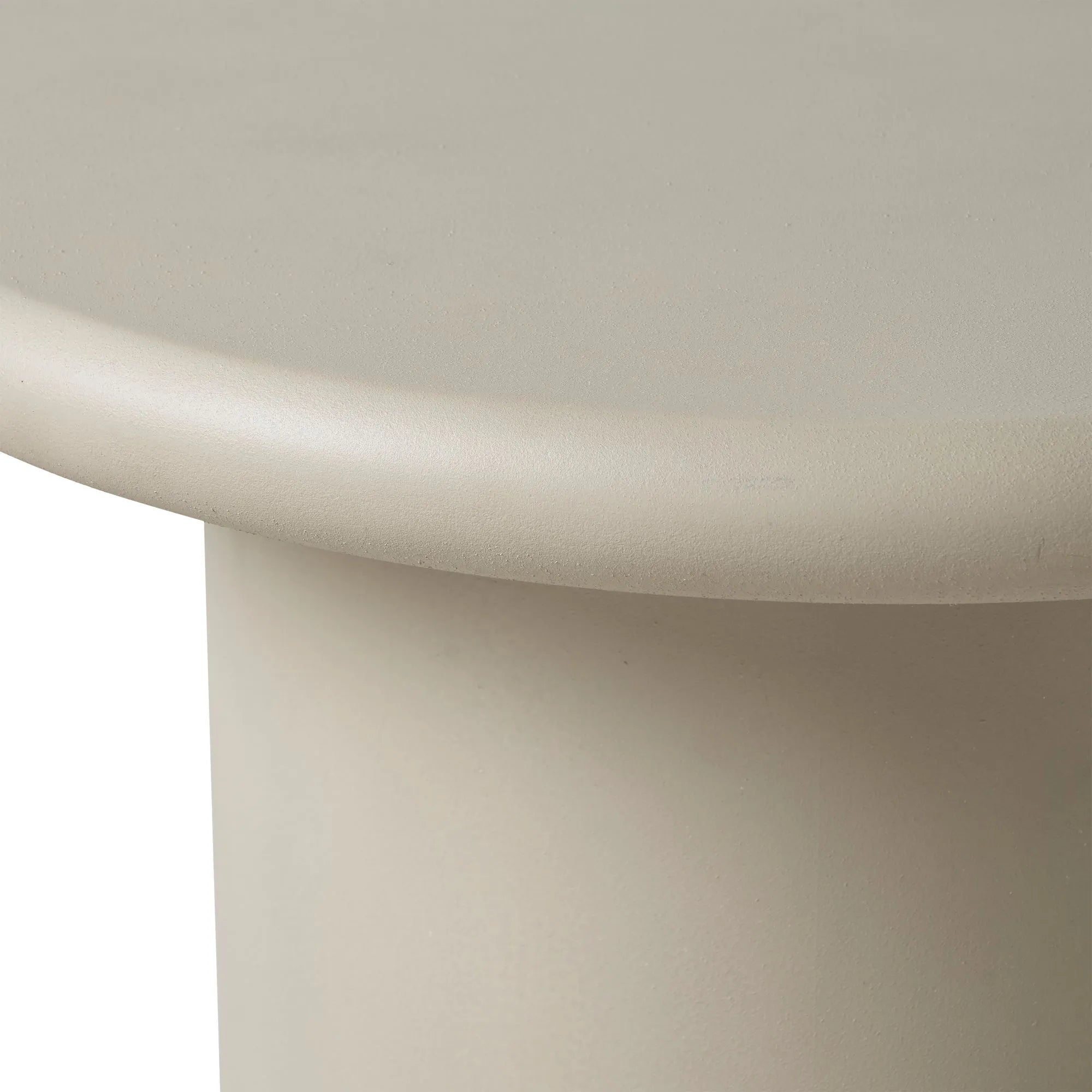 Close-up of the rounded edge of Riya, a smooth, light beige cylindrical accent table against a white background—perfect for minimalist interiors.
