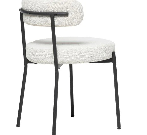 The Stacy Chair is a modern dining chair with a round, padded white seat and backrest on a minimalist black metal frame with four slender legs, shown from an angled rear view.